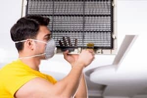 Technician in a mask performing HVAC system maintenance, inspecting air conditioning unit components for optimal performance.