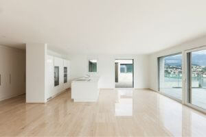 Empty modern house interior with large windows and polished wooden floors, emphasizing the need for optimal thermostat settings during summer months when unoccupied.
