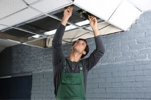 Technician inspecting and repairing HVAC unit in ceiling, addressing potential leaks and maintenance issues.