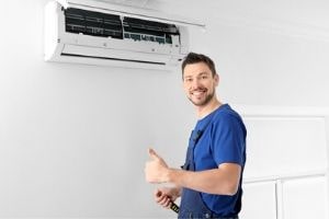 HVAC technician giving a thumbs up next to a wall-mounted air conditioning unit, emphasizing professional furnace repair services and safety in home heating systems.