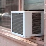 Window-mounted air conditioner with holiday decorations on a brick building by Atlantic Heating & Air Conditioning.