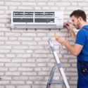 HVAC technician servicing wall-mounted ductless mini split AC unit while woman watches