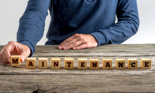 Person arranging wooden blocks spelling "MAINTENANCE" on a rustic table, emphasizing the importance of HVAC maintenance for homeowners.