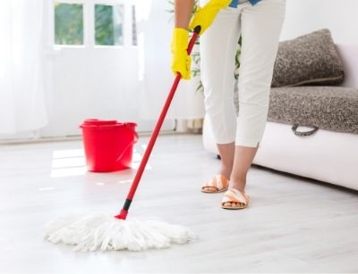 Person mopping a clean floor with a red bucket nearby, emphasizing spring cleaning benefits for maintaining a healthy home environment and supporting AC system efficiency.