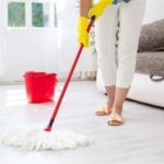 Person cleaning light-colored floors with a white mop and red bucket, highlighting home maintenance for HVAC systems.