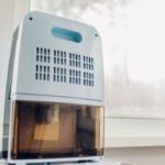 Modern dehumidifier in a bright home, featuring a water collection bucket and ventilation grilles for optimal air quality.