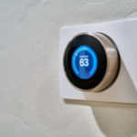 Wall-mounted thermostat with digital display at 63°F, sleek circular design with blue light for HVAC efficiency.
