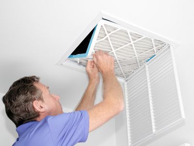 Man replacing air filter in ceiling air vent, emphasizing importance of regular maintenance for HVAC efficiency and comfort.