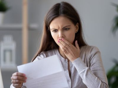Woman looking shocked while reading a document, illustrating concerns related to air conditioning maintenance and repair signs.