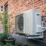 Contemporary air conditioning unit on brick wall with potted plant, highlighting efficient HVAC solutions for home heating.