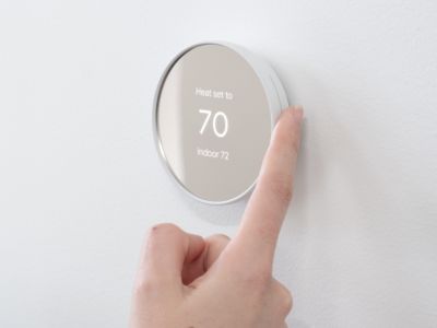 Smart thermostat displaying temperature settings with a hand adjusting the controls, illustrating energy efficiency and home comfort solutions for heating and cooling.