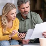 A man and woman discussing energy-saving tips for HVAC systems with a laptop and smartphone in a bright indoor setting.