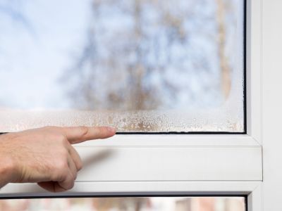 Hand pointing at condensation on a window, illustrating signs of excess humidity and potential need for a dehumidifier in home environments.