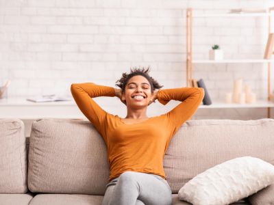 Smiling woman relaxing on a couch, enjoying comfortable indoor air quality enhanced by proper humidity levels.