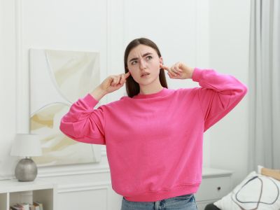 Woman in a pink sweatshirt covering her ears, expressing discomfort from loud sounds, related to air conditioning issues.