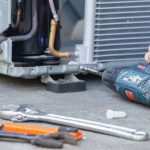 Technician servicing an air conditioning unit with tools like a drill and wrenches for HVAC maintenance and repairs.