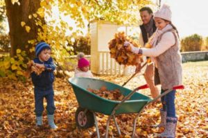Family raking autumn leaves, preparing yard for winter, showcasing seasonal outdoor maintenance.