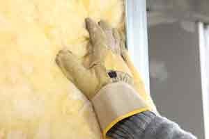 Hand wearing a glove pressing against insulation material, illustrating home insulation techniques for energy efficiency in Boston homes.