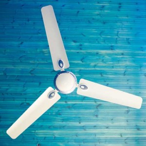 Ceiling fan with three white blades against a blue wooden background, illustrating cooling solutions for summer HVAC maintenance.